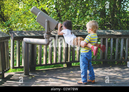 Jeune garçon (4-5) aider girl (2-3) looking through telescope Banque D'Images