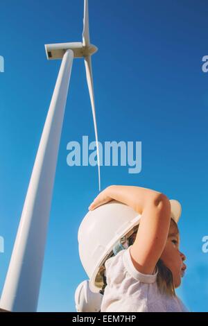 Fille portant un casque de sécurité debout sous une éolienne, États-Unis Banque D'Images