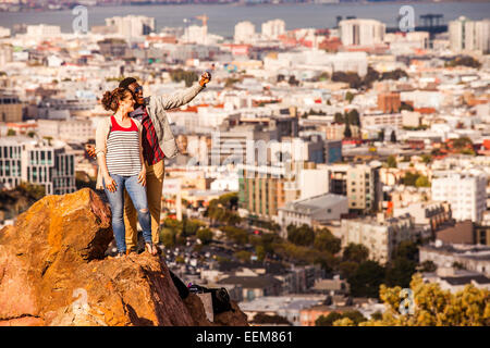 Couple qui selfies téléphone cellulaire sur rocher surplombant une vue panoramique du paysage urbain Banque D'Images