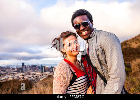 Couple smiling on grassy hill donnant sur cityscape Banque D'Images