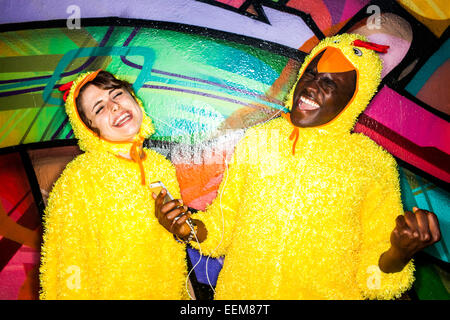 Couple en costumes identiques à l'écoute près de mur de graffiti écouteurs Banque D'Images