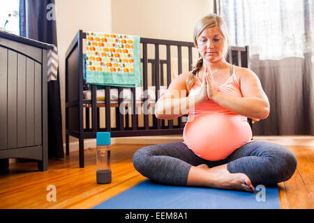 Pregnant Caucasian woman meditating in nursery Banque D'Images