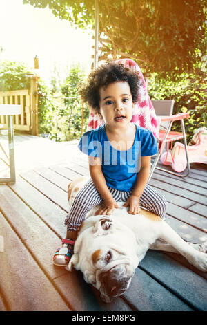 Mixed Race girl sitting on dog on porch Banque D'Images