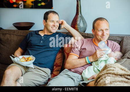 Young gay couple relaxing on sofa with baby boy Banque D'Images