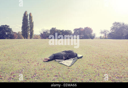 Sieste sur l'homme en manteau sur le terrain du parc Banque D'Images