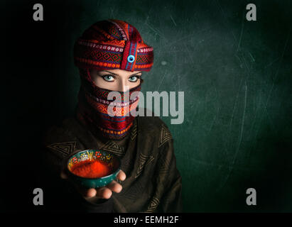 Femme orientale en turban rouge offrant le chili en poudre au green textured wall Banque D'Images