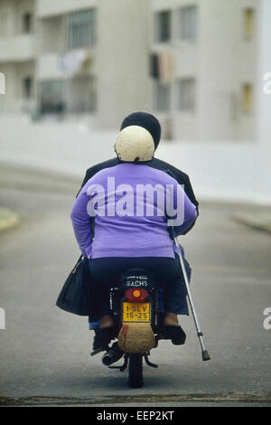 Une femme handicapée avec une béquille à cheval sur le dos d'un scooter. Le Portugal. Banque D'Images