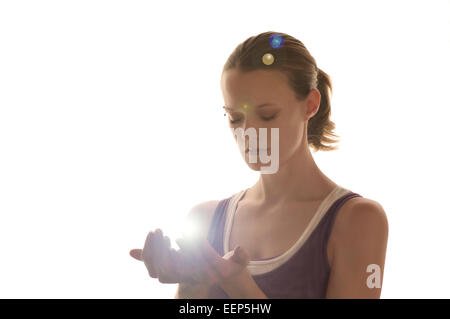 Belle jeune femme les yeux fermer détient ses mains prenant une boule de lumière lumineuse elle porter un débardeur violet et blanc. Banque D'Images