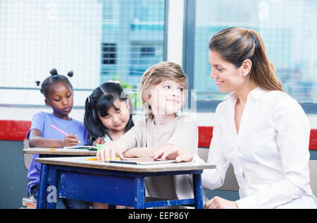 Kid l'apprentissage d'utilisation tablet avec l'enseignant avec ses camarades de livres à colorier. Concept classe multiraciale. Banque D'Images