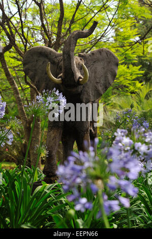 Brown bull charge sculpture éléphant africain, décoration de jardin entouré de plantes vertes et de fleurs violettes en parterre Banque D'Images