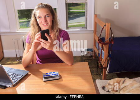 Élève ayant une déficience visuelle à l'aide de son téléphone portable dans sa chambre d'étudiant Banque D'Images
