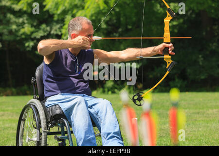 L'homme avec de la moelle épinière en fauteuil roulant visant son arc et flèche de tir à l'arc pratique Banque D'Images