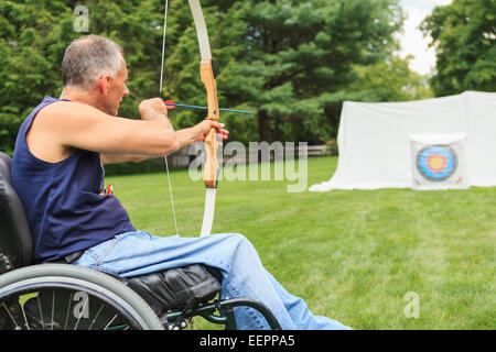 L'homme avec de la moelle épinière en fauteuil roulant visant son arc et flèche de tir à l'arc pratique Banque D'Images