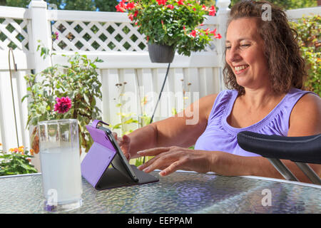 Femme avec le spina-bifida sur patio travaillant sur tablet Banque D'Images