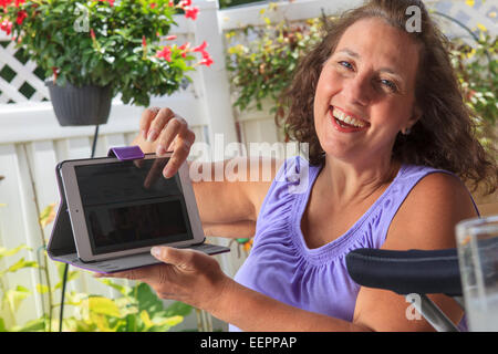 Femme avec le spina-bifida sur patio travaillant sur tablet Banque D'Images