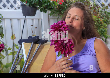 Femme avec le spina-bifida sentant les fleurs sur le patio du jardin Banque D'Images