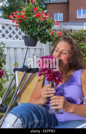 Femme avec le spina-bifida sentant les fleurs sur le patio du jardin Banque D'Images