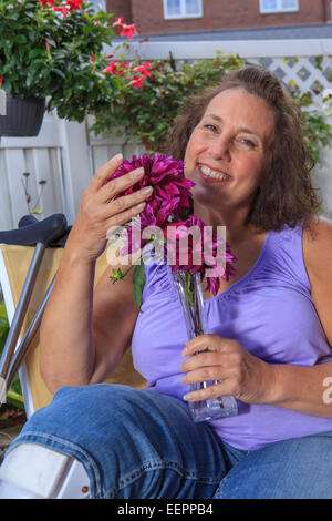 Femme avec le spina-bifida sentant les fleurs sur le patio du jardin Banque D'Images