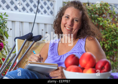 Femme avec le spina-bifida Rédaction de notes tout en vous relaxant sur patio Banque D'Images