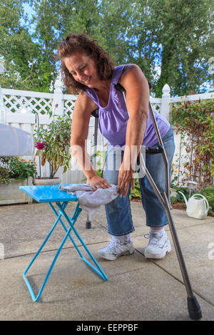 Femme avec le spina-bifida nettoyage table patio avec des béquilles Banque D'Images