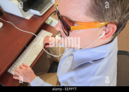 L'homme avec la cécité congénitale en utilisant la technologie d'assistance à son ordinateur pour écouter Banque D'Images