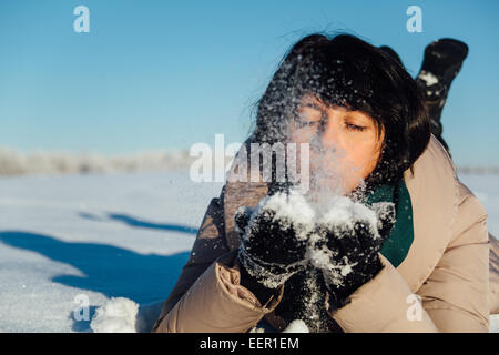 Girl lying on the snow et souffle la neige des mains Banque D'Images