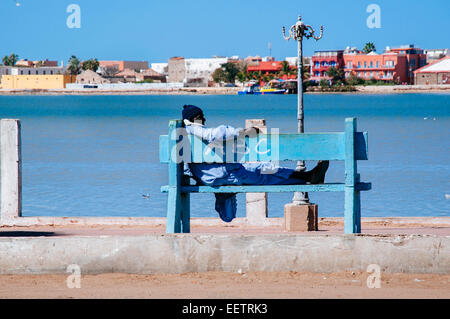 Vieil homme assis sur un banc, dans les rues de Saint Louis du Sénégal avec la rivière à l'arrière, le Sénégal. Banque D'Images