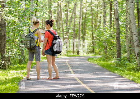 Deux amies debout sur une piste cyclable dans la forêt et en regardant une carte Banque D'Images