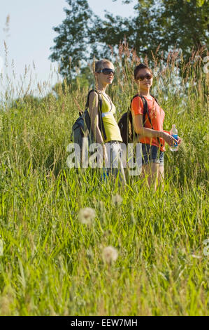 Deux amies de la randonnée à travers la tenue d'herbe de l'eau en bouteille Banque D'Images