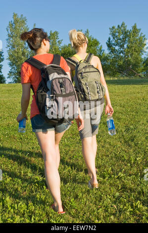 Fille de deux amis marchant dans l'herbe vers les arbres Banque D'Images