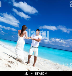 Heureux jeunes mariés en robes blanches s'amusant sur la plage avec une mer turquoise background Banque D'Images