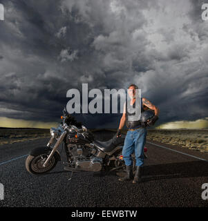 Old biker sur une longue route avec les nuages de tempête Banque D'Images