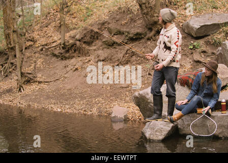 Jeune couple dans une forêt, à la pêche dans une rivière. Banque D'Images