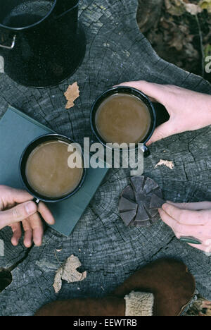 Couple having coffee in a forest, deux tasses de café, une cafetière et une paire de gants sur un tronc d'arbre. Banque D'Images