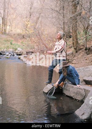 Jeune couple dans une forêt, à la pêche dans une rivière. Banque D'Images