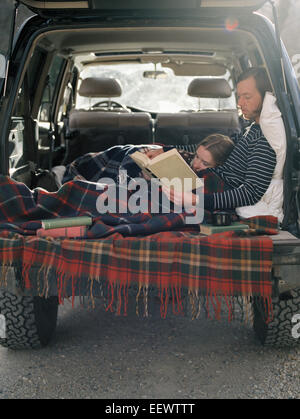 Jeune couple couché dans l'arrière de leur voiture, la lecture d'un livre. Banque D'Images