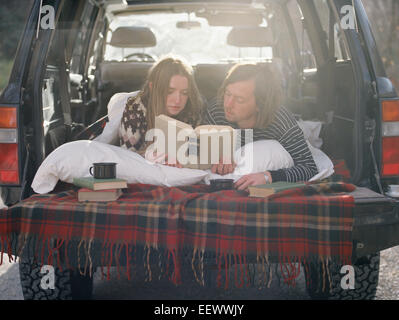 Jeune couple couché dans l'arrière de leur voiture, la lecture d'un livre. Banque D'Images