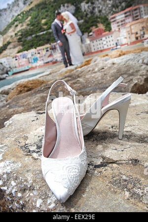 Mariée et le marié, baiser sur le brise-lames en pierre à Gibraltar avec le Catalan Bay village en arrière-plan et de chaussures de mariage en premier plan Banque D'Images