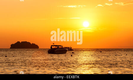 Silhouette d'une petite île et de petit bateau au coucher du soleil. Banque D'Images