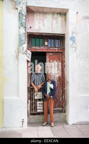 Deux personnes âgées debout à la porte d'une porte d'un petit magasin délabré délabrés avec peeling peinture in urban Camaguey, Cuba Banque D'Images