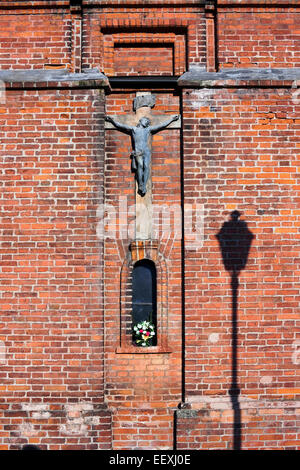 Le bronze ancien crucifixion du Christ se bloque sur un mur de brique rouge. Journée ensoleillée Banque D'Images