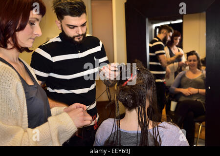 Les jeunes stagiaires, hommes et femmes qui travaillent sur les coiffeurs cheveux tressage d'une clientèle féminine dans un salon Banque D'Images