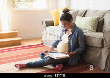 Pregnant woman sitting on floor reading book Banque D'Images