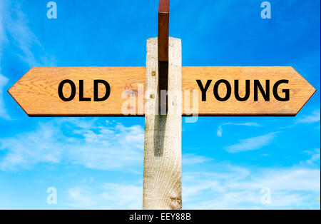 Panneau en bois avec deux flèches opposées sur ciel bleu clair, les travailleurs âgés par rapport aux jeunes des messages Banque D'Images