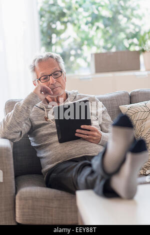 Senior man sitting on sofa in living room and using tablet pc Banque D'Images