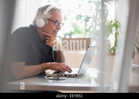 Senior man sitting in office portant des écouteurs et using laptop Banque D'Images