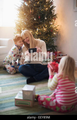 Mère avec enfants (4-5, 6-7) l'ouverture des cadeaux de Noël et de prendre des photos Banque D'Images