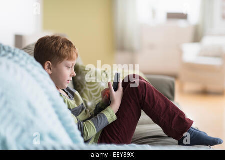 Boy (6-7) sitting on couch et using cell phone Banque D'Images