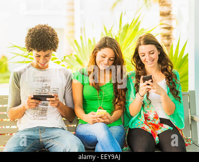 USA, Jupiter, en Floride, Groupe d'amis (14-15) assis sur un banc et texting Banque D'Images