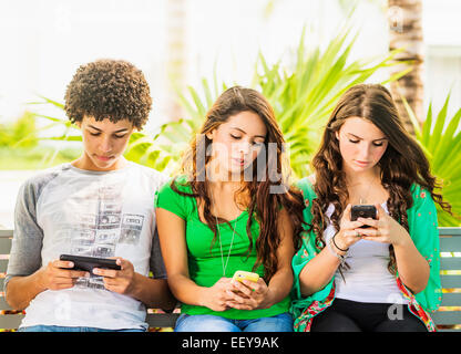 USA, Jupiter, en Floride, Groupe d'amis (14-15) assis sur un banc et texting Banque D'Images